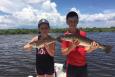 Two kids on a boat hold fish they caught.