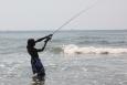 A boy casting with his fishing pole while wading in the water on Elmer's Island beach.