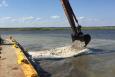 Excavator bucket distributing oyster cultch off of a barge. Photo: Covington Civil and Environmental, LLC