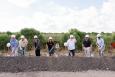 seven men and women stand in hardhats holding shovels at a groundbreaking ceremony