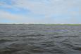 Open water of Barataria Bay with a strip of dunes and beach in the background.