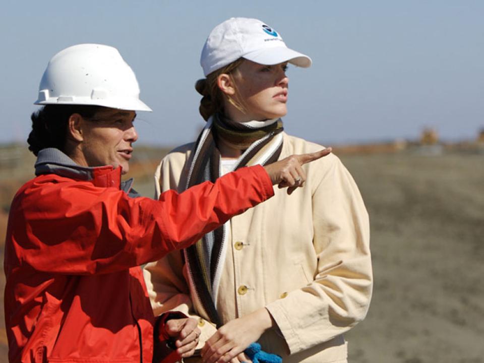 Two people standing outside, one is wearing a hard hat and pointing