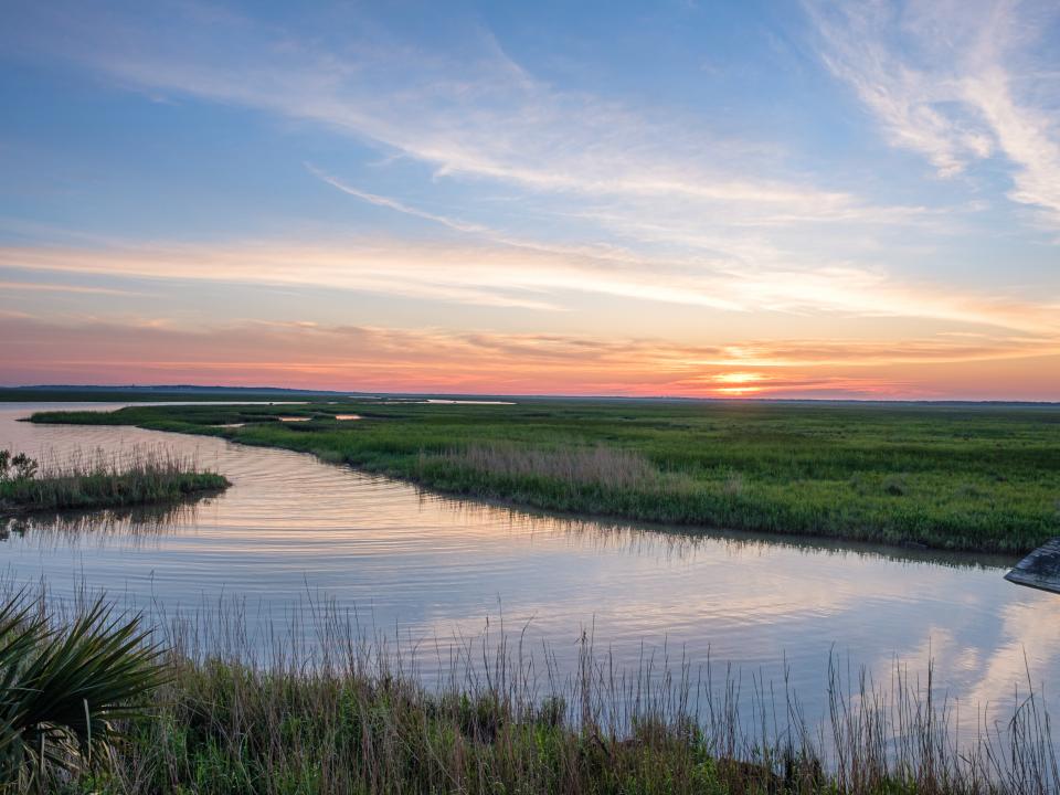 calm water sits amongst green grass with a sunset sky