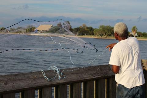 A recreational angler tosses a net out off a fishing pier.
